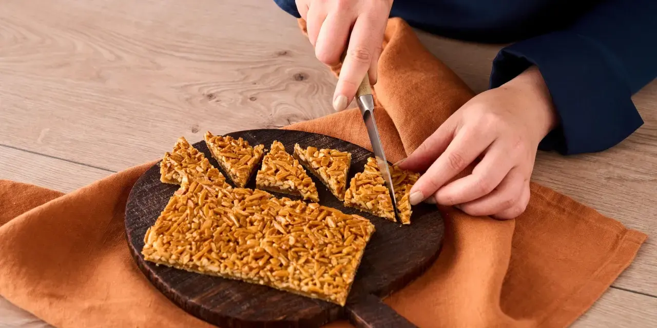 Ein Nussecken Rezept wird hier gezeigt. Eine Person schneidet die süßen Nussecken auf einem Holzbrett.