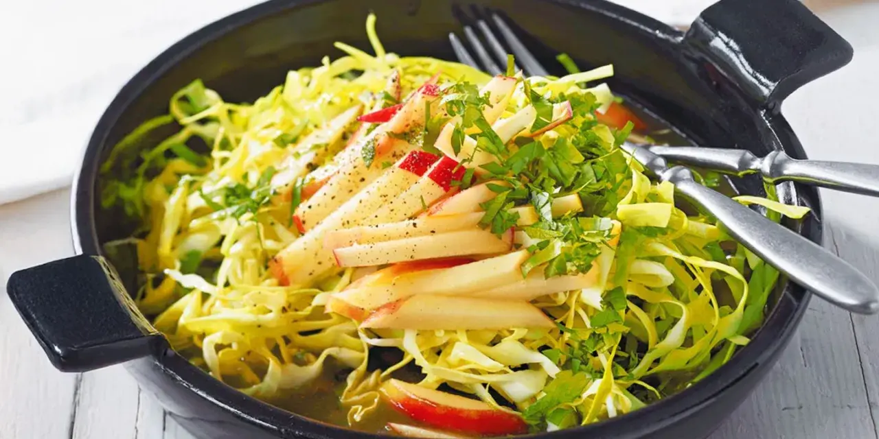 Frischer Spitzkohl Salat mit Apfelspalten und Kräutern, appetitlich in einer schwarzen Schüssel serviert.