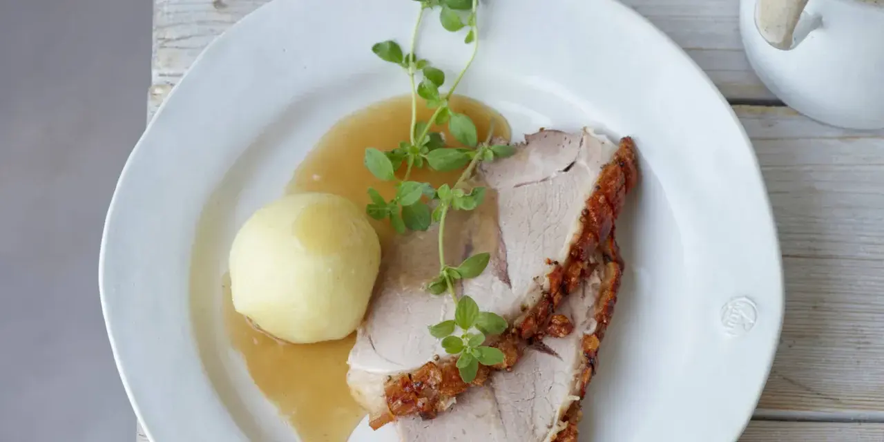 Ein knuspriger Schweinebraten mit Soße und Klößen, perfekt für ein deftiges Schweinebraten Rezept. Frisch garniert mit Kräutern.