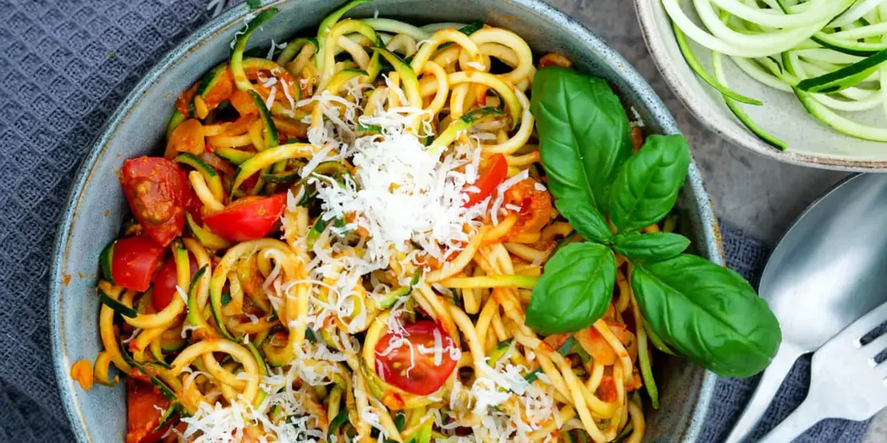 Herzhafte Zucchini-Nudeln mit Tomaten und Basilikum, bestreut mit Parmesan. Ein leichter Genuss!