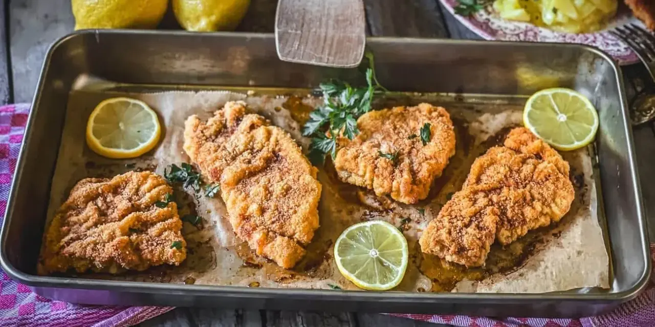 Saftiges Schnitzel im Backofen, goldbraun paniert, mit frischer Petersilie und Zitronenspalten garniert. Ein Genuss!