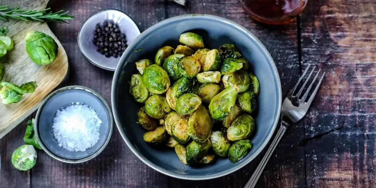 Gerösteter Rosenkohl in einer Schüssel, bereit für leckere Rezepte mit Rosenkohl. Daneben Salz, Pfeffer und ein Glas Sirup.