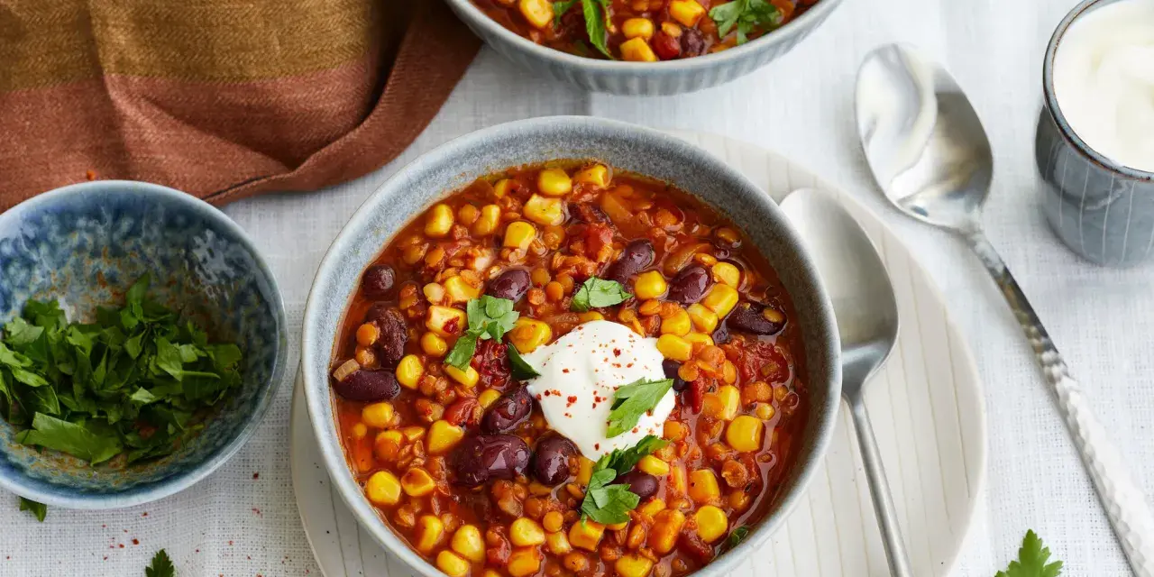 Herzhaftes Chili sin Carne mit Mais, Bohnen und Linsen, garniert mit einem Klecks Sauerrahm und frischer Petersilie.
