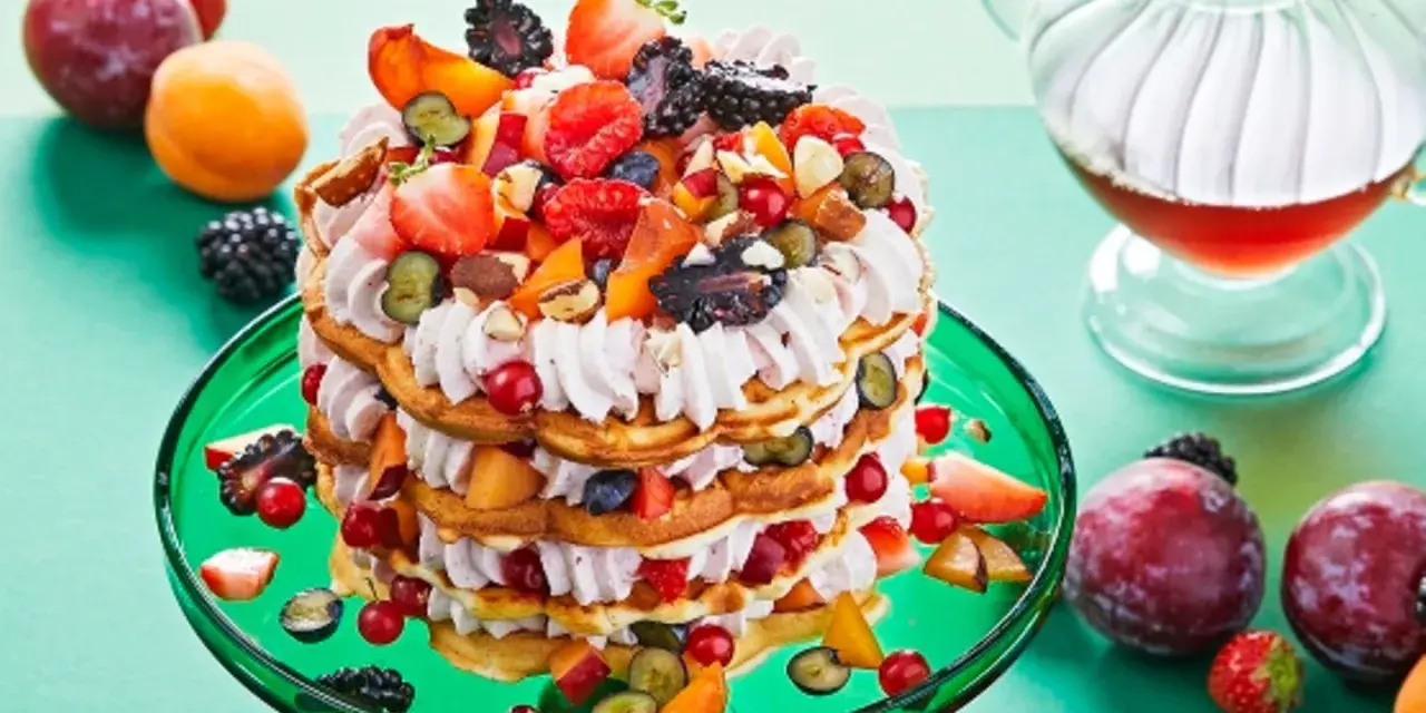 Eine mehrstöckige Waffeltorte mit Mascarpone-Creme, Beeren, Pfirsichen und Nüssen, garniert mit frischen Früchten.