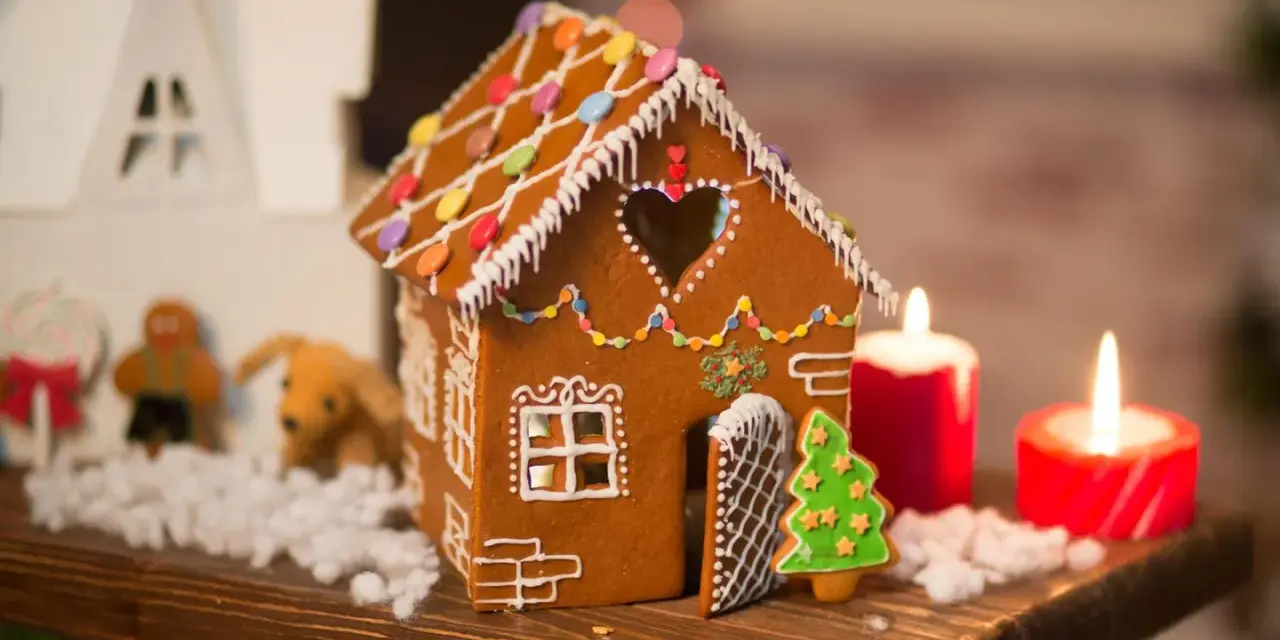 Ein zauberhaftes Lebkuchenhaus, das Lust macht, es selber zu machen. Verziert mit bunten Smarties und Zuckerguss, steht es neben Kerzen und Weihnachtsfiguren.