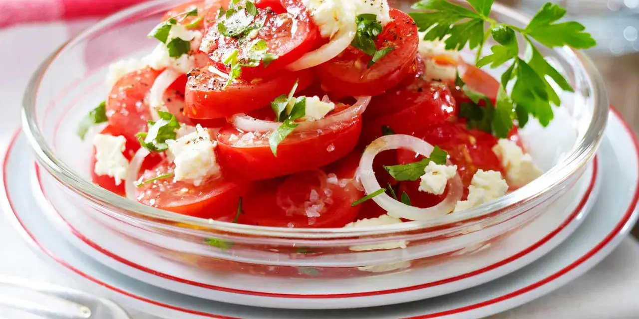 Frischer Tomaten Feta Salat mit Zwiebelringen und Petersilie, garniert mit schwarzem Pfeffer und Meersalz.