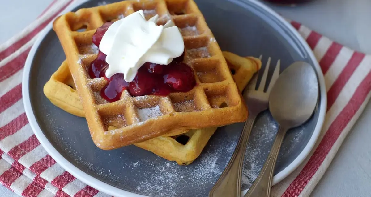 Zwei Hefewaffeln mit Trockenhefe, garniert mit Kirschkompott und Sahne, bestäubt mit Puderzucker.