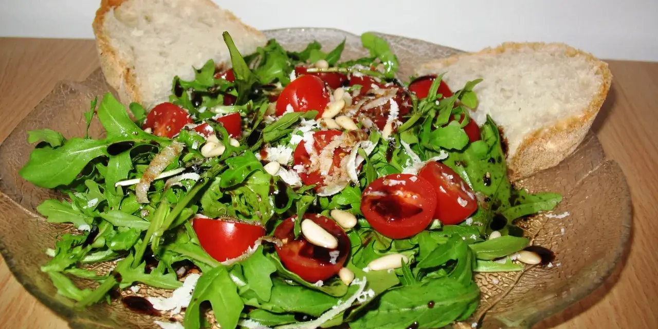 Frischer Rucola Salat mit Kirschtomaten, Pinienkernen und Parmesan, beträufelt mit Balsamico-Dressing. Dazu knuspriges Brot.