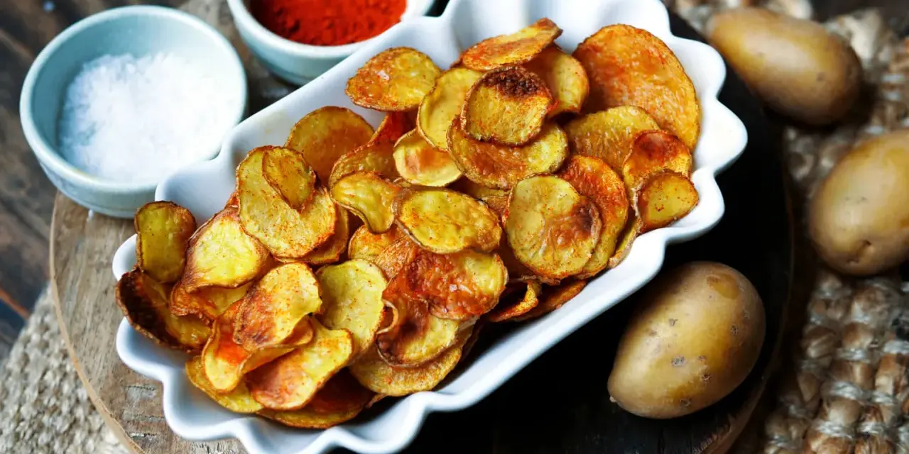 Selbstgemachte Kartoffelchips, goldbraun und knusprig, mit Salz und Paprikapulver daneben. So einfach kannst du Chips selber machen!