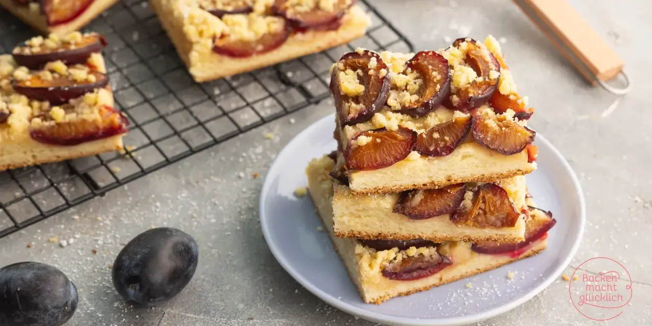 Saftiger zwetschgenkuchen vegan mit Streuseln auf einem Teller gestapelt. Daneben frische Zwetschgen und ein Kuchenblech.