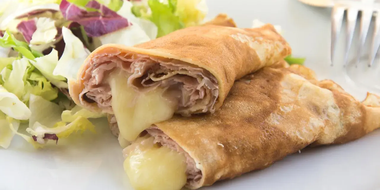 Zwei herzhafte Pfannkuchen mit Schinken und geschmolzenem Käse, serviert mit einem frischen Salat.