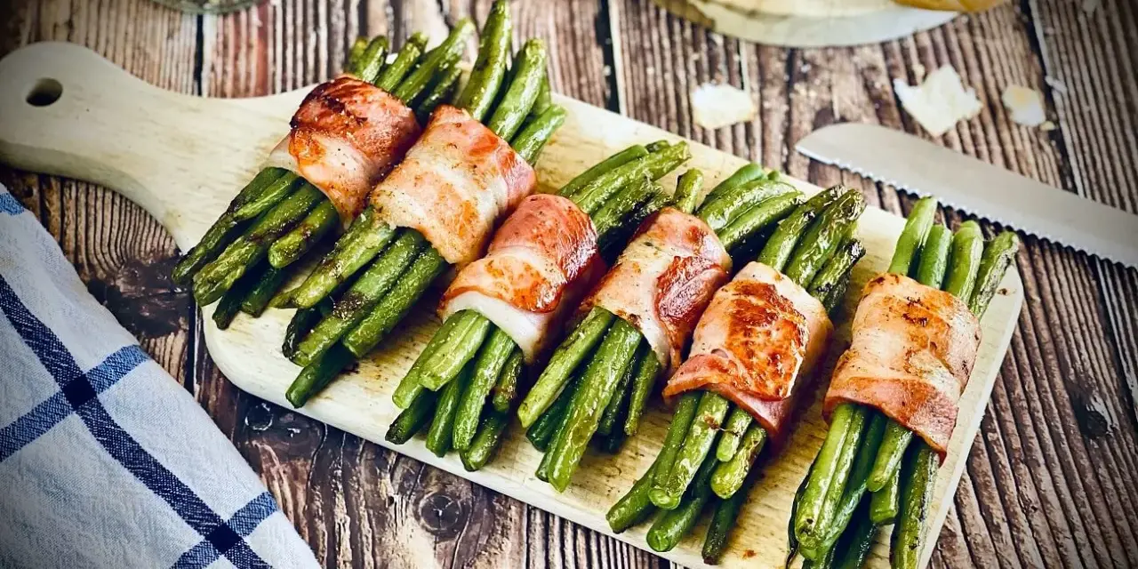 Grüne Bohnen, umwickelt mit knusprigem Speck, ein köstliches Speckbohnen Rezept, serviert auf einem Holzbrett.