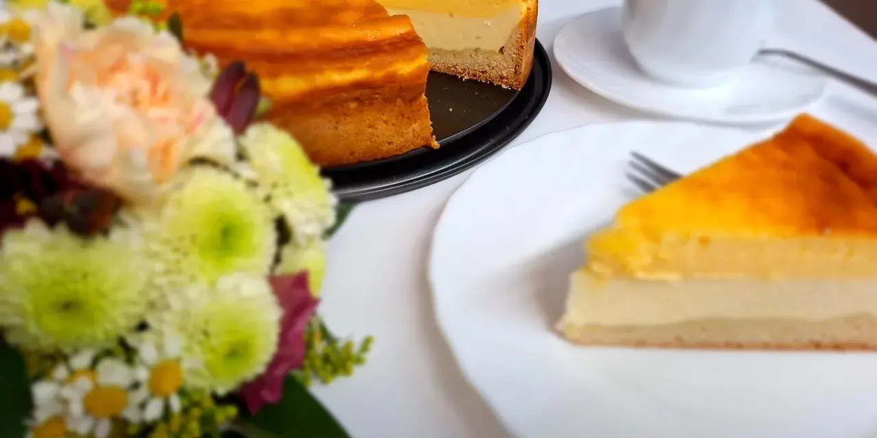 Ein köstliches Eierschecke-Rezept: Ein goldbrauner Kuchen mit cremiger Füllung, daneben eine Tasse Kaffee und ein Blumenstrauß.