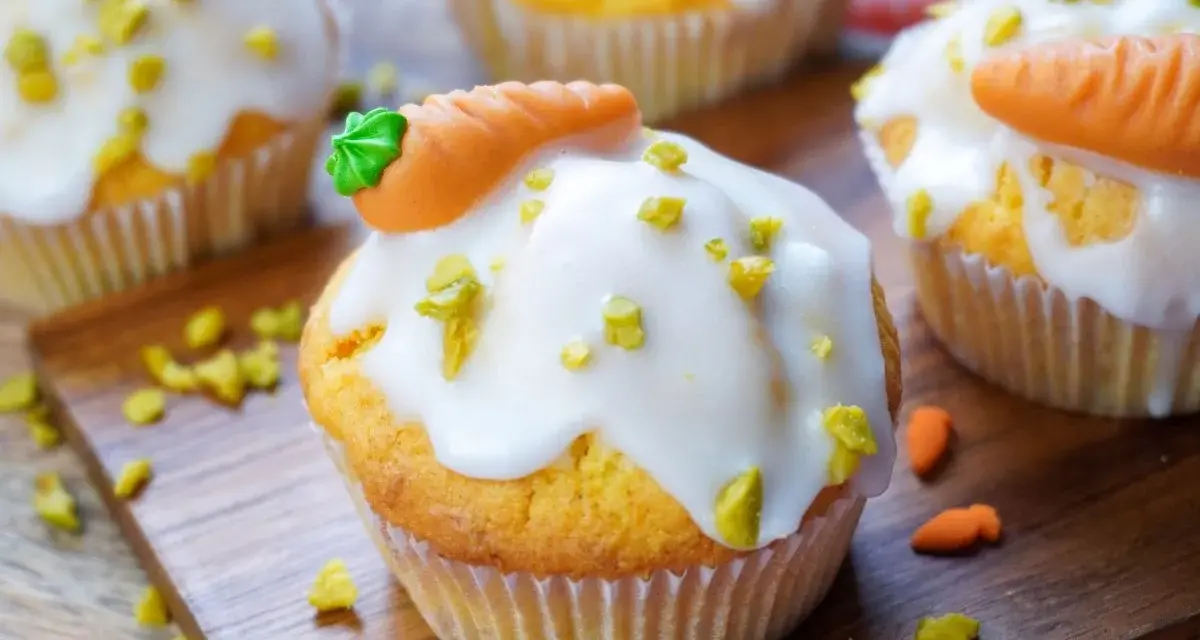Leckere Karotten Muffins mit weißer Glasur und Marzipan-Karotten, bestreut mit gehackten Pistazien.