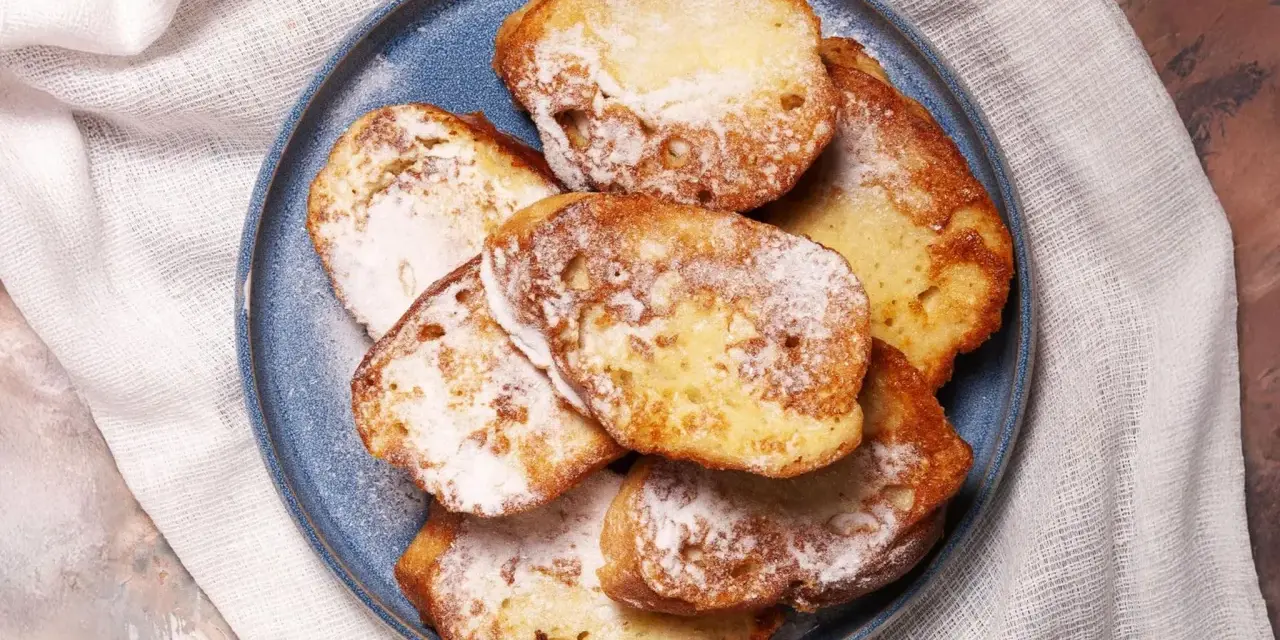 Armer Ritter, goldbraun gebacken und mit Puderzucker bestäubt, liegen auf einem blauen Teller.