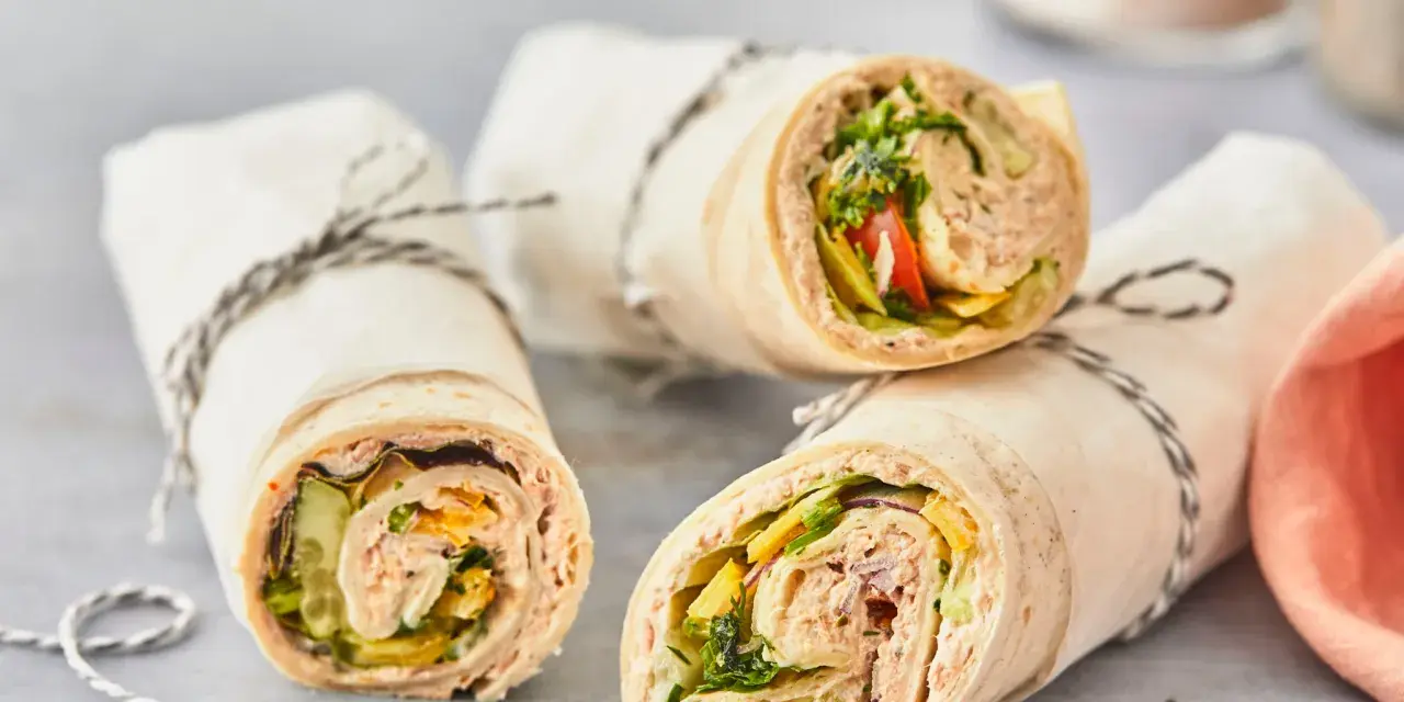Drei leckere Thunfisch-Wraps, gefüllt mit Salat, Gurke und Tomate, sind in Papier gewickelt und mit Schnur verschnürt.