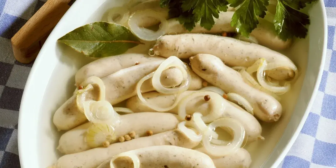 Saure Zipfel in einer Schüssel mit Zwiebelringen, Lorbeerblatt und Petersilie.