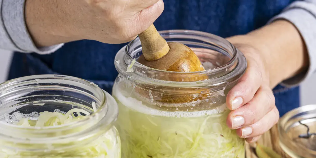 Hände pressen Kohl für ein einfaches Sauerkraut Rezept in ein Glas.