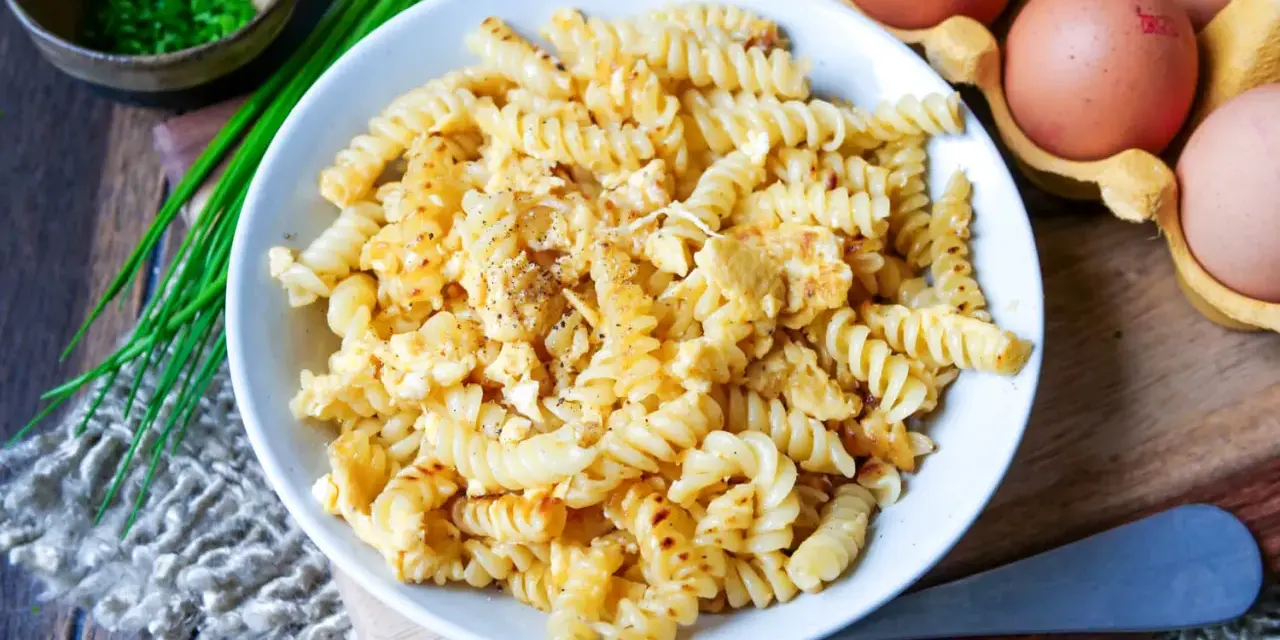Fusilli-Nudeln mit Rührei, bestreut mit Pfeffer. Daneben liegen frische Eier und Schnittlauch. Ein einfaches Gericht: Nudeln mit Ei.