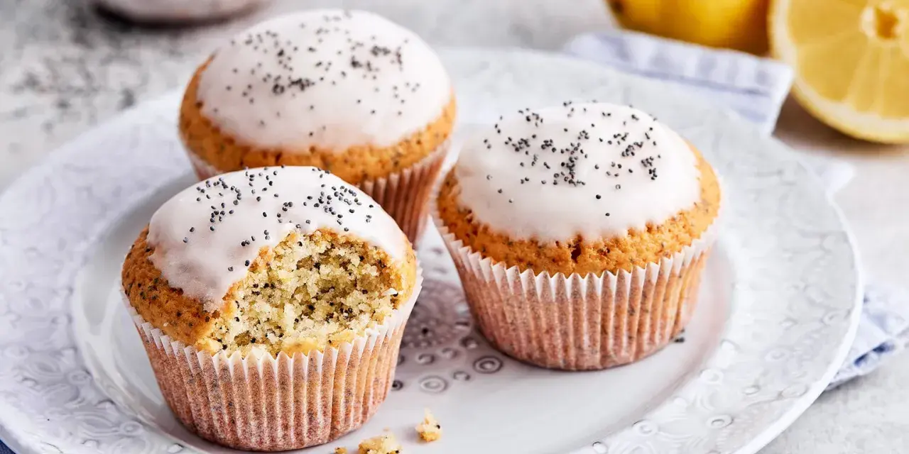 Drei köstliche zitronen mohn muffins mit Zuckerguss und Mohn bestreut, daneben frische Zitronen.