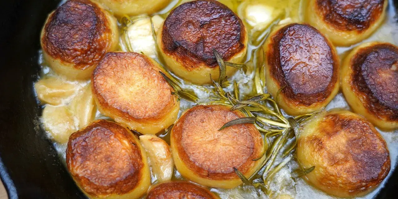 Goldbraun gebratene Fondant-Kartoffeln mit Rosmarin und Knoblauch in einer Pfanne.