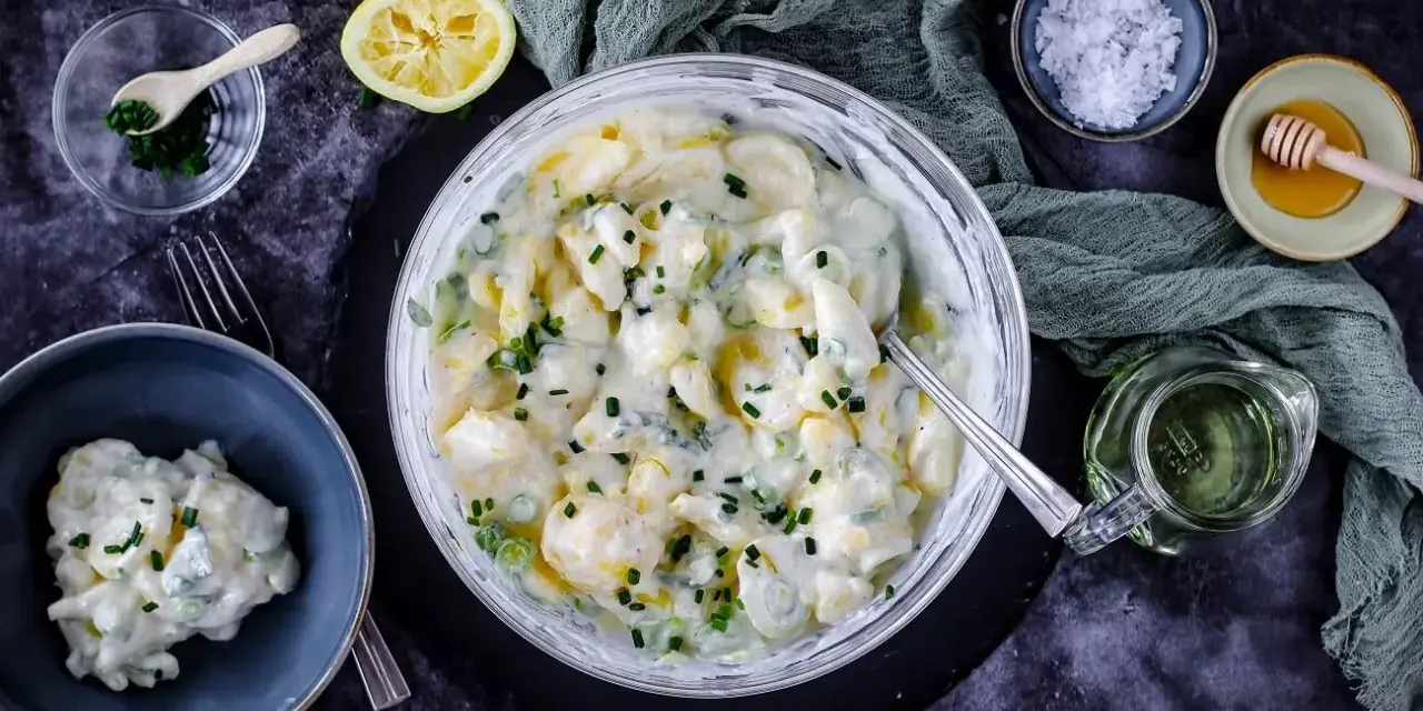 Cremiger Kartoffelsalat mit Joghurt, garniert mit Schnittlauch. Dazu Zitrone, Honig und grobes Salz.