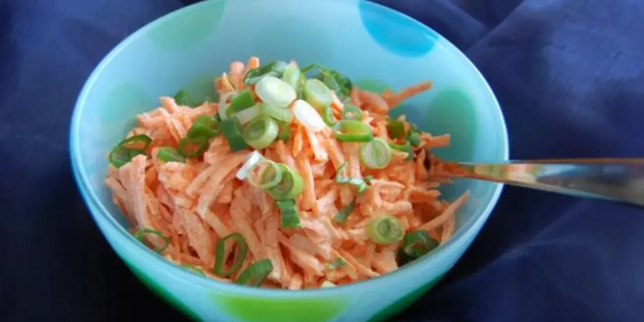 Karottensalat mit cremigem karottensalat dressing und Frühlingszwiebeln in einer bunten Schüssel.