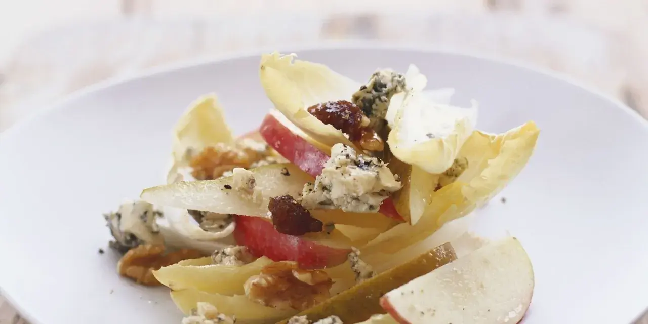 Ein köstlicher chicoree salat mit Äpfeln, Birnen, Blauschimmelkäse und Walnüssen auf einem weißen Teller.