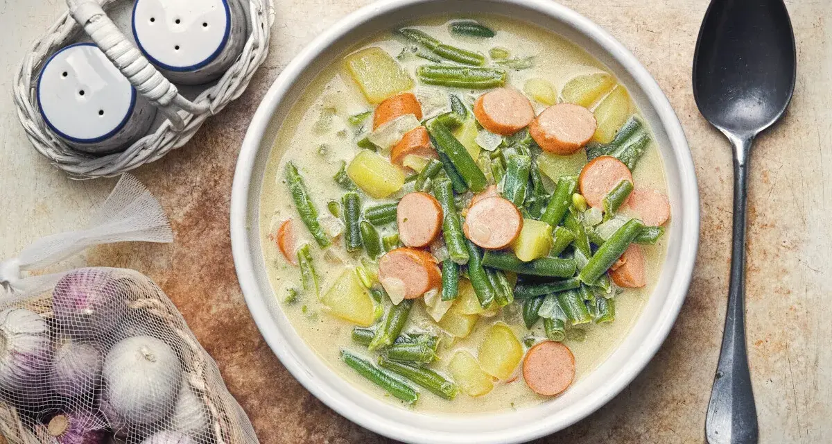 Herzhafte Bohnen-Kartoffel-Suppe mit Würstchen, ein Klassiker unter den Bohnen Rezepten. Dazu Salz- und Pfefferstreuer und frischer Knoblauch.
