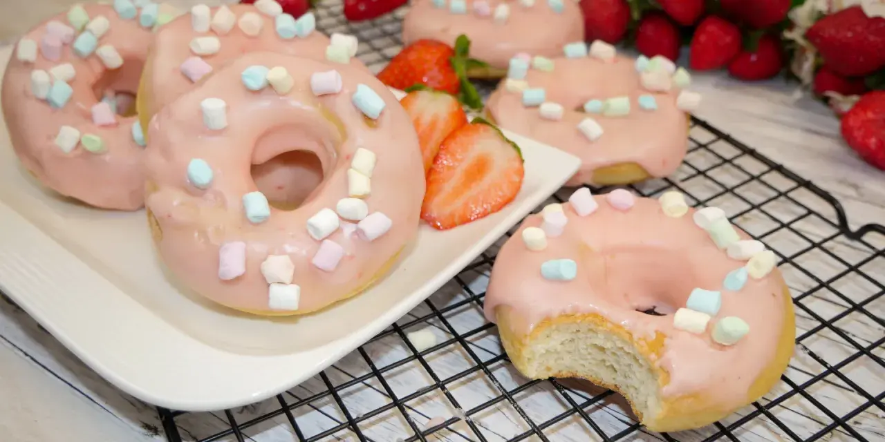 Leckere Donuts mit rosa Glasur und Marshmallows, perfekt für ein schnelles Donuts Rezept aus dem Backofen. Frische Erdbeeren garnieren das süße Gebäck.