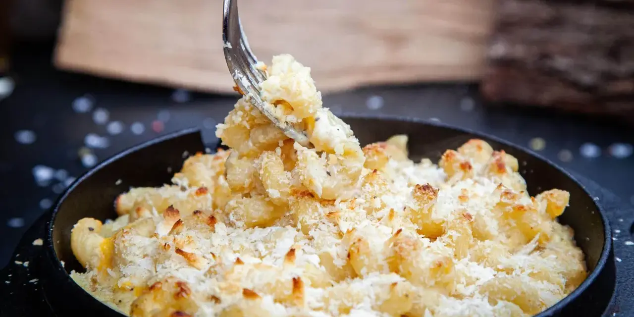 Ein Gabel hebt cremiges, überbackenes Mac n Cheese aus einer Pfanne. Dieses amerikanische Original-Rezept ist ein Genuss!