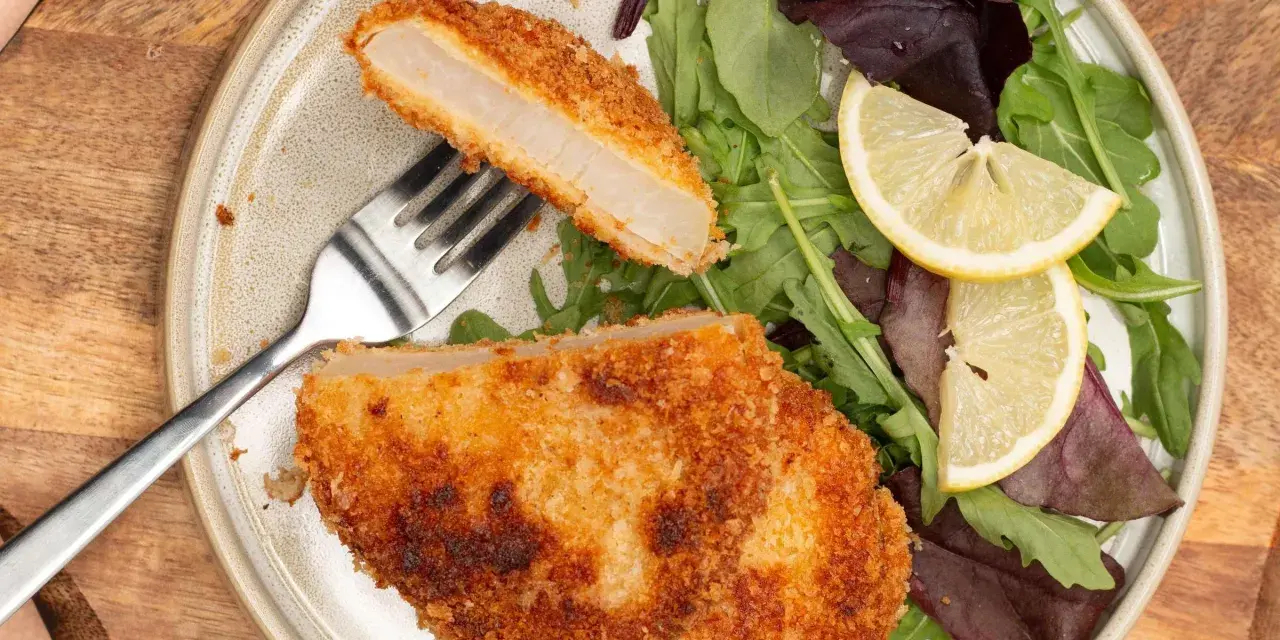 Knuspriges Kohlrabi-Schnitzel mit Salat und Zitrone auf einem Teller.
