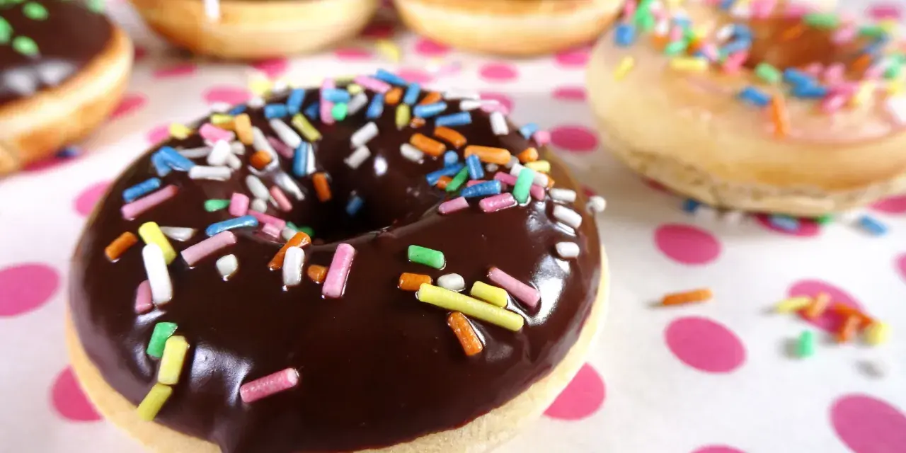 Bunte Streusel auf Schokoladen- und Zuckerguss-Donuts, die an ein leckeres Donut Teig Rezept erinnern.