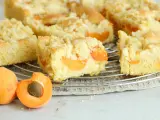 Saftiger aprikosenkuchen mit Streuseln, frisch gebacken und auf einem Gitterrost abgekühlt. Daneben liegen zwei saftige Aprikosen.
