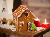 Ein zauberhaftes Lebkuchenhaus, das Lust macht, es selber zu machen. Verziert mit bunten Smarties und Zuckerguss, steht es neben Kerzen und Weihnachtsfiguren.