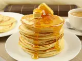 Ein Stapel goldbrauner Pancakes, übergossen mit Honig und Butter, daneben eine Tasse Kaffee. Perfekt für ein leckeres Pancakes Rezept.
