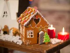 Ein zauberhaftes Lebkuchenhaus, das Lust macht, es selber zu machen. Verziert mit bunten Smarties und Zuckerguss, steht es neben Kerzen und Weihnachtsfiguren.