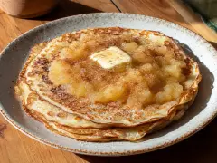 Ein Stapel goldbrauner Pfannkuchen, belegt mit Apfelmus, Zimt und einem Stück Butter. Ein köstliches Pfannkuchen Rezept für jeden Tag.
