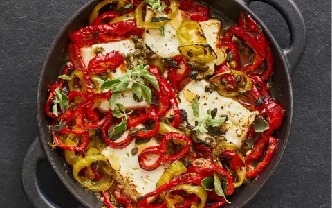 Gebackener Feta mit bunten Paprikastreifen, Kapern und frischen Kräutern in einer gusseisernen Pfanne.