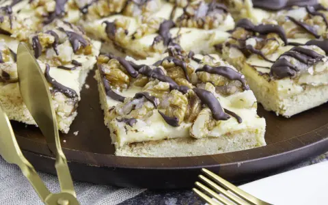 Ein "friss dich dumm kuchen" mit cremiger Füllung, Walnüssen und Schokoladendrizzle auf einem Holztablett. Goldene Gabel und Messer liegen daneben.