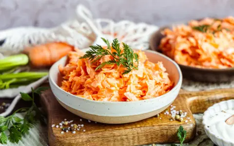 Karottensalat mit cremigem Dressing, wie im Restaurant. Frisch geriebene Karotten, garniert mit Dill, auf einem Holzbrett.