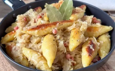 Schupfnudeln mit Sauerkraut, Speck und Lorbeerblättern in einer Pfanne. Ein herzhaftes Gericht, das zum Genießen einlädt.