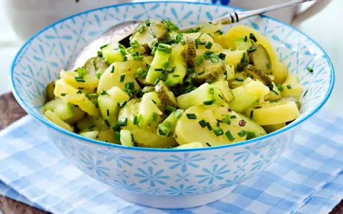 Schüssel mit Kartoffelsalat mit Gurken und Schnittlauch, garniert mit frischen Kräutern.