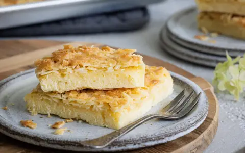 Zwei Stücke saftiger Butterkuchen mit knuspriger Mandelkruste auf einem Teller, bereit zum Genießen. Ein köstliches butterkuchen rezept.