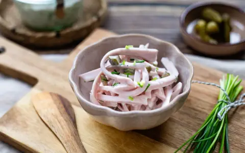 Schmackhaftes Fleischsalat-Rezept mit Gurkenstückchen und Schnittlauch garniert, serviert in einer Schale auf einem Holzbrett.
