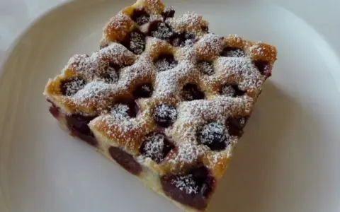 Zwei Stücke Kirschstreuselkuchen vom Blech, mit Puderzucker bestäubt, auf einem weißen Teller.