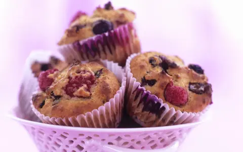 Saftige Muffins mit Obst und Joghurt, garniert mit frischen Himbeeren und Blaubeeren, in einem rosa Körbchen.
