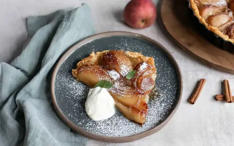 Ein Stück Quitten Tarte Tatin, bestäubt mit Puderzucker und garniert mit Sahne und Minze.