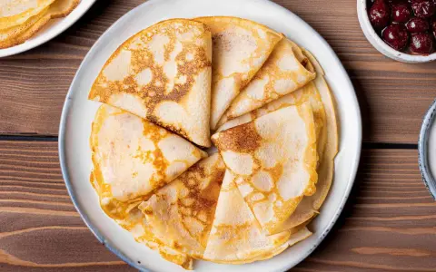 Omas Pfannkuchen-Rezept: goldbraune, gefaltete Pfannkuchen auf einem Teller, daneben eine Schüssel mit Kirschen.
