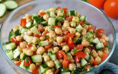 Frischer Kichererbsen Salat mit Gurken, Tomaten und Kräutern in einer Glasschüssel. Ein leichter und gesunder Genuss.